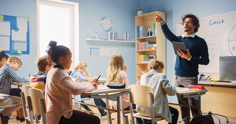 Male teacher being animated in front of a class of primary students