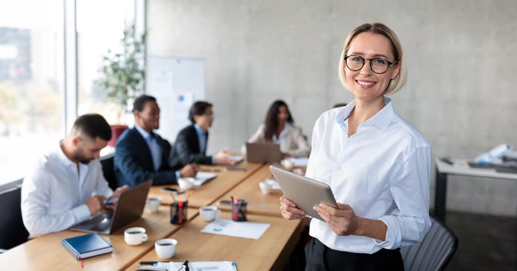 Standing professional woman holding tablet in meeting