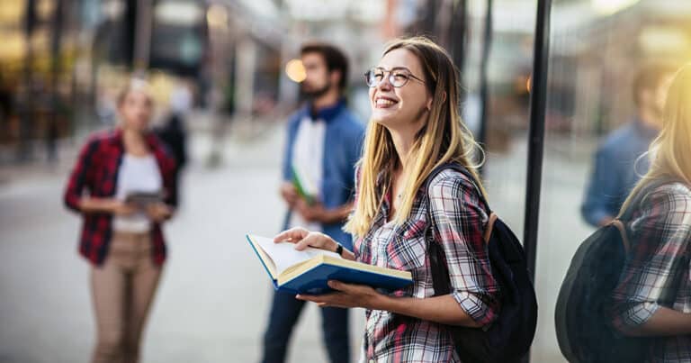 Young woman standing outside urban building holding a book